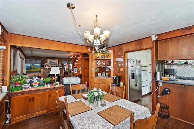 dining area featuring stairs, wooden walls, a chandelier, and dark wood-type flooring