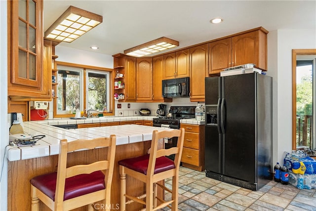 kitchen featuring a kitchen breakfast bar, kitchen peninsula, tile counters, and black appliances
