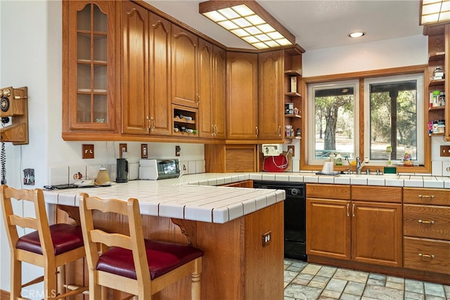 kitchen with kitchen peninsula, sink, dishwasher, tile counters, and a breakfast bar area
