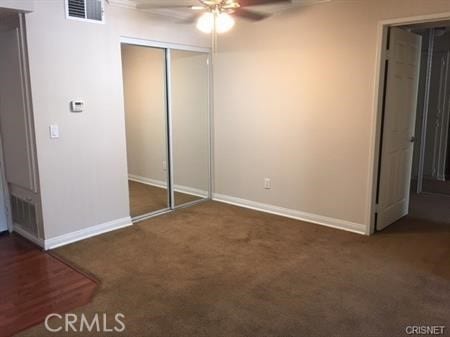 unfurnished bedroom with a closet, dark colored carpet, and ceiling fan