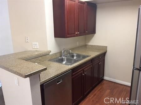 kitchen featuring dark hardwood / wood-style floors, sink, kitchen peninsula, stainless steel appliances, and light stone countertops