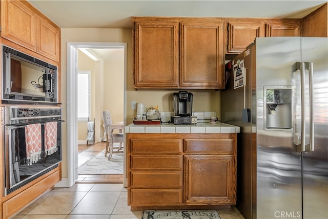 kitchen with black appliances, light tile patterned flooring, and tile counters