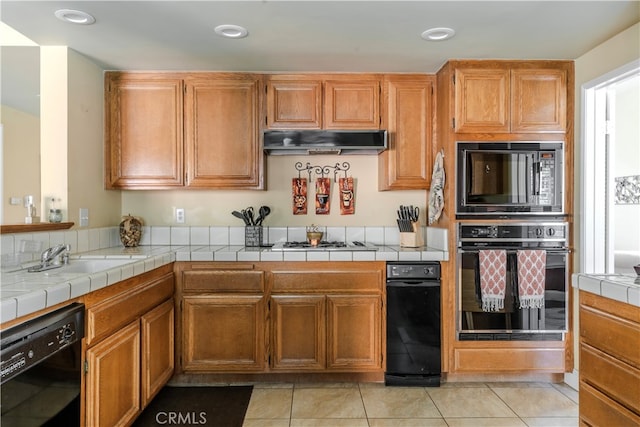 kitchen with light tile patterned flooring, sink, tile counters, and black appliances