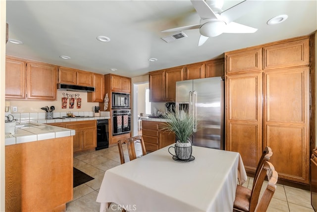 kitchen featuring appliances with stainless steel finishes, light tile patterned floors, ceiling fan, tile counters, and sink