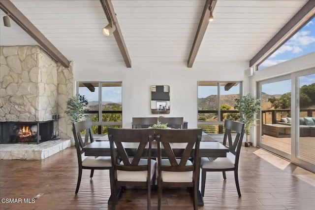 dining space with a mountain view, beamed ceiling, dark wood-type flooring, a high ceiling, and a fireplace