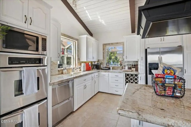 kitchen with light stone counters, stainless steel appliances, vaulted ceiling, and white cabinetry