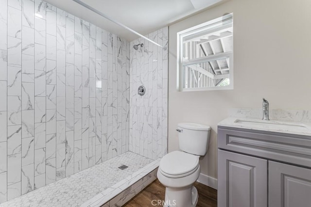 bathroom with hardwood / wood-style floors, vanity, toilet, and a tile shower