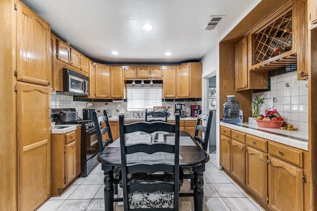 kitchen featuring tile countertops, gas stove, light tile patterned flooring, and backsplash