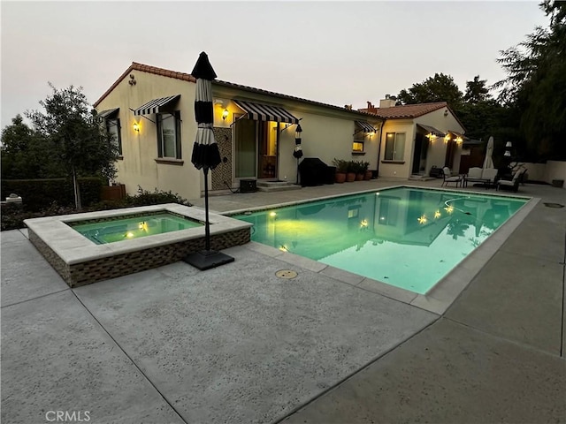 pool at dusk featuring an in ground hot tub and a patio area