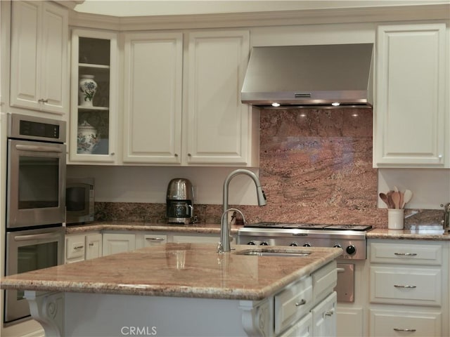 kitchen with appliances with stainless steel finishes, wall chimney exhaust hood, light stone counters, and white cabinetry