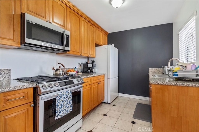 kitchen with light stone countertops, sink, light tile patterned floors, and appliances with stainless steel finishes