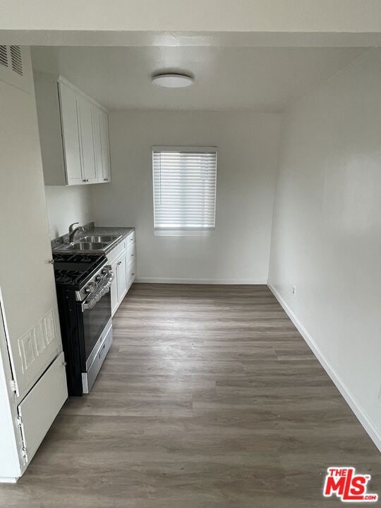 kitchen with sink, stainless steel gas stove, white cabinets, and dark wood-type flooring