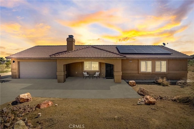 back house at dusk featuring a patio, a garage, and solar panels