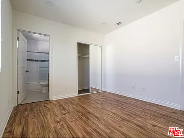 unfurnished bedroom featuring connected bathroom, a closet, and hardwood / wood-style floors