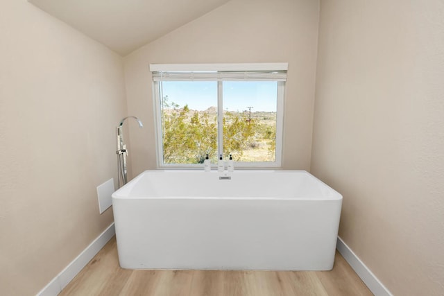 bathroom featuring wood-type flooring, vaulted ceiling, and a tub