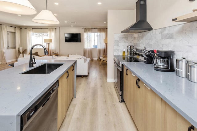 kitchen featuring appliances with stainless steel finishes, hanging light fixtures, light stone counters, sink, and wall chimney range hood