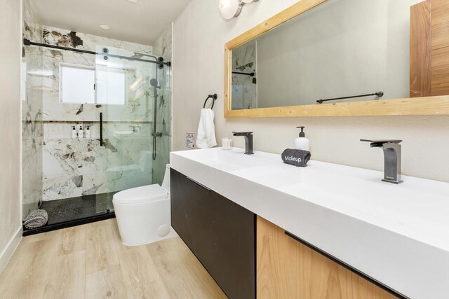 bathroom featuring wood-type flooring, a shower with door, vanity, and toilet