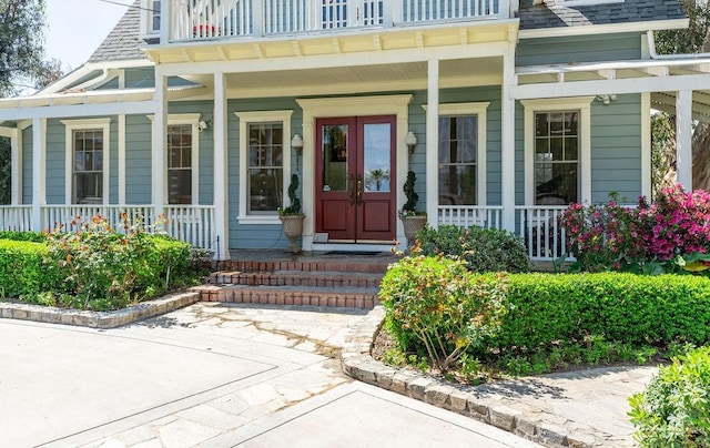 property entrance featuring a porch, a balcony, and french doors