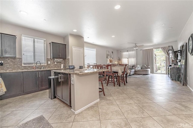 kitchen with ceiling fan, a center island, sink, light stone counters, and light tile patterned floors