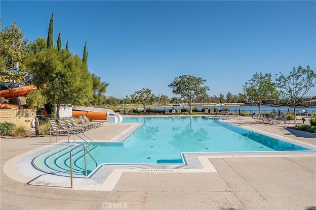 view of swimming pool featuring a water slide, a patio area, and a water view