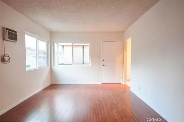 empty room with hardwood / wood-style flooring, a textured ceiling, and a wall unit AC