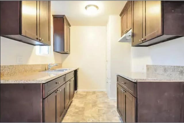 kitchen with dark brown cabinets, light stone counters, and sink