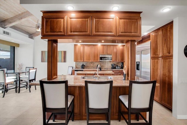 kitchen with backsplash, beam ceiling, a breakfast bar, appliances with stainless steel finishes, and light stone counters