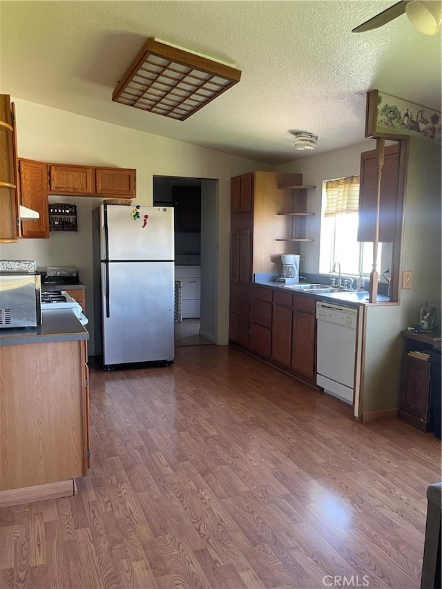 kitchen featuring dishwasher, sink, stainless steel fridge, light wood-type flooring, and a textured ceiling