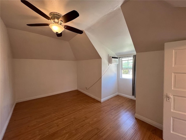 additional living space featuring lofted ceiling, hardwood / wood-style floors, a wall mounted air conditioner, and ceiling fan