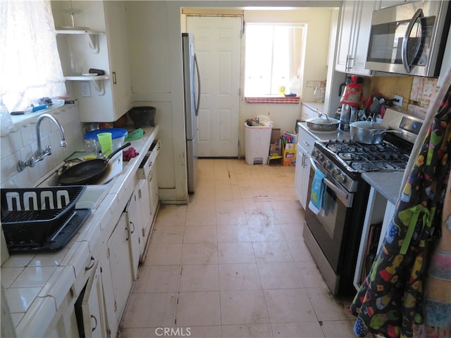 kitchen featuring tile countertops, white cabinets, stainless steel appliances, and backsplash