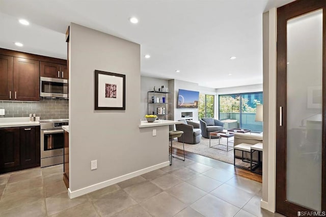 kitchen with a kitchen bar, backsplash, dark brown cabinets, stainless steel appliances, and light tile patterned floors