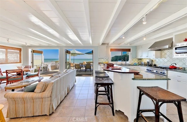 kitchen with white cabinetry, wall chimney exhaust hood, rail lighting, a breakfast bar, and a water view