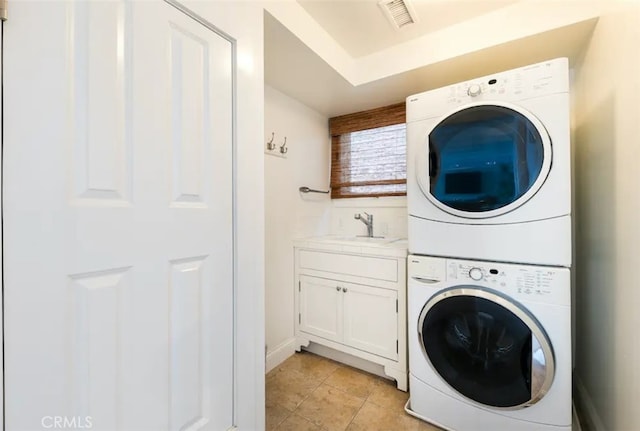 laundry area featuring cabinets, light tile patterned flooring, stacked washer and clothes dryer, and sink