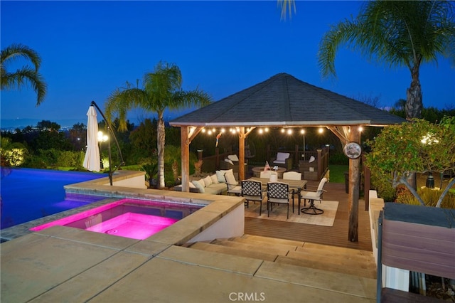 pool at twilight featuring a gazebo, a deck, and an in ground hot tub