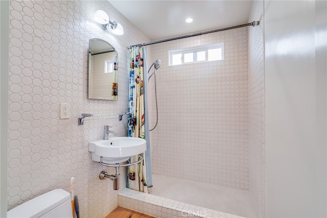 bathroom with a shower with shower curtain, toilet, sink, and tile walls