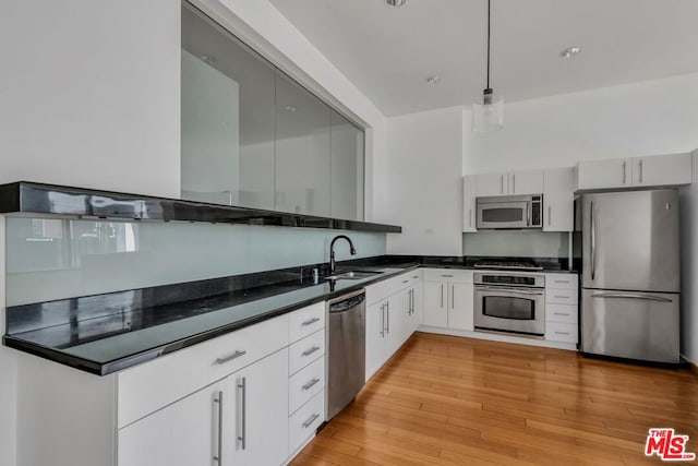 kitchen with white cabinetry, light hardwood / wood-style floors, sink, stainless steel appliances, and pendant lighting