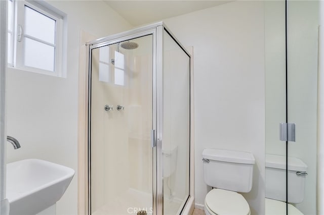 bathroom featuring toilet, a shower with door, and sink