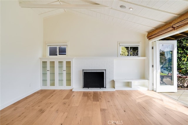 unfurnished living room with beam ceiling, light hardwood / wood-style floors, and a brick fireplace