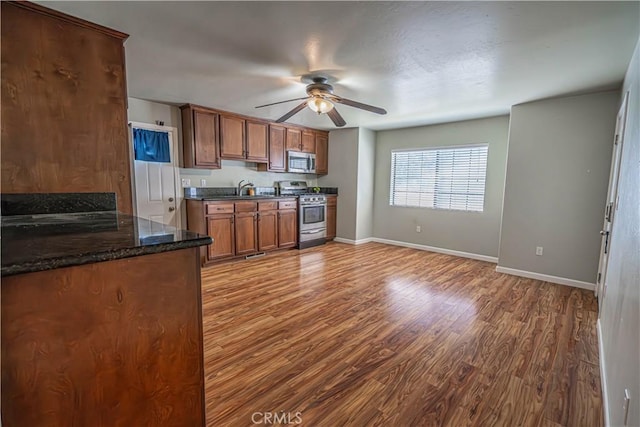 kitchen with sink, hardwood / wood-style flooring, ceiling fan, dark stone countertops, and appliances with stainless steel finishes