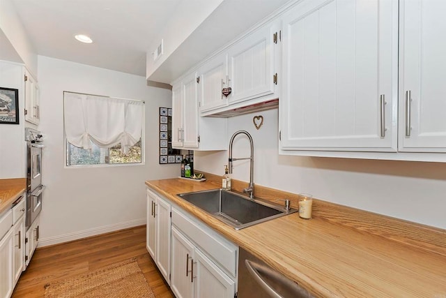 kitchen featuring oven, white cabinets, sink, and light hardwood / wood-style floors