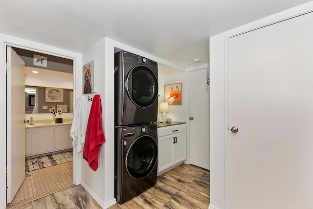 clothes washing area with cabinets, light hardwood / wood-style flooring, sink, and stacked washing maching and dryer