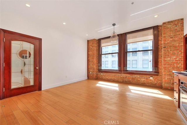 unfurnished living room featuring brick wall and light hardwood / wood-style floors