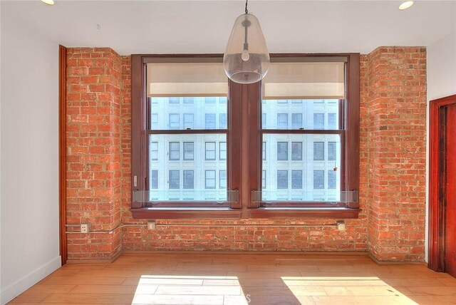 unfurnished dining area featuring brick wall and light wood-type flooring