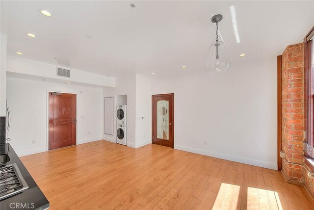 unfurnished living room featuring light hardwood / wood-style floors and stacked washer / drying machine