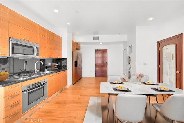 kitchen with sink, light wood-type flooring, a kitchen breakfast bar, stacked washer and clothes dryer, and stainless steel appliances