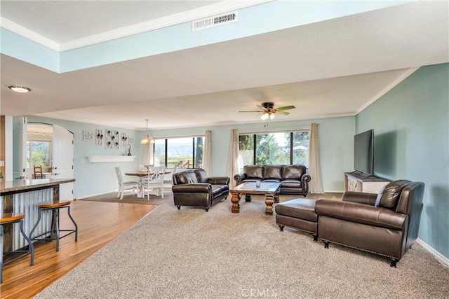 living room with ceiling fan, visible vents, arched walkways, wood finished floors, and ornamental molding