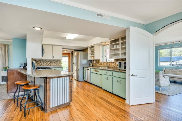 kitchen with visible vents, open shelves, a peninsula, a sink, and appliances with stainless steel finishes