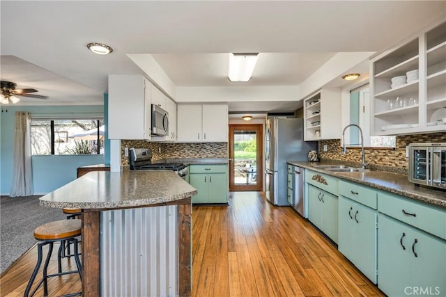 kitchen with a healthy amount of sunlight, appliances with stainless steel finishes, open shelves, a sink, and a peninsula