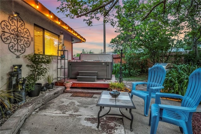 patio terrace at dusk featuring fence and a hot tub
