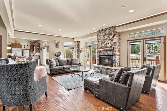 living room featuring french doors, wood-type flooring, crown molding, and a stone fireplace